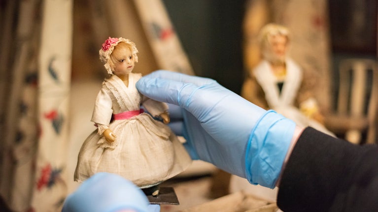 Close-up of gloved hand cleaning a doll in the 18th century doll's house at Nostell Priory, West Yorkshire